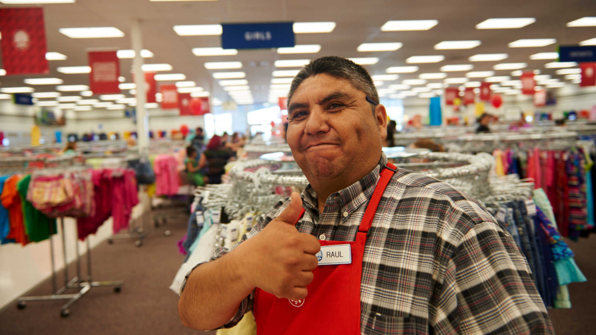 A male DI associate flashes a thumbs up as he goes about his work in the clothing section.